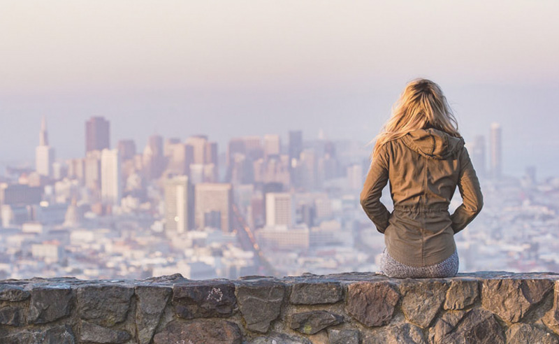 Nő dombon ülve a várost nézi.