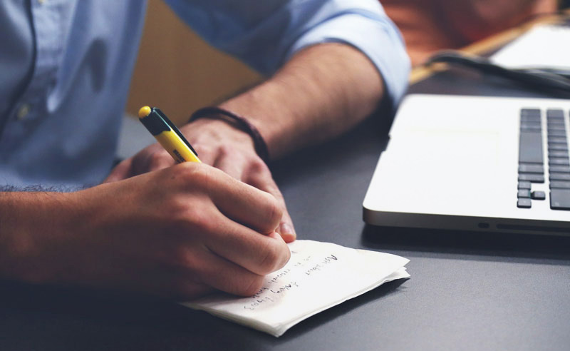 Férfi laptop mellett papírra jegyzetel