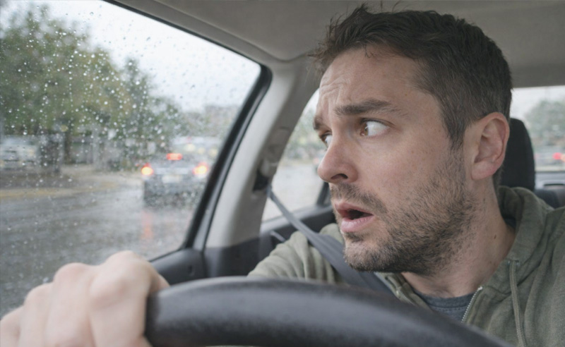 Férfi esős időben jobbkezes utcából érkező autót figyeli.