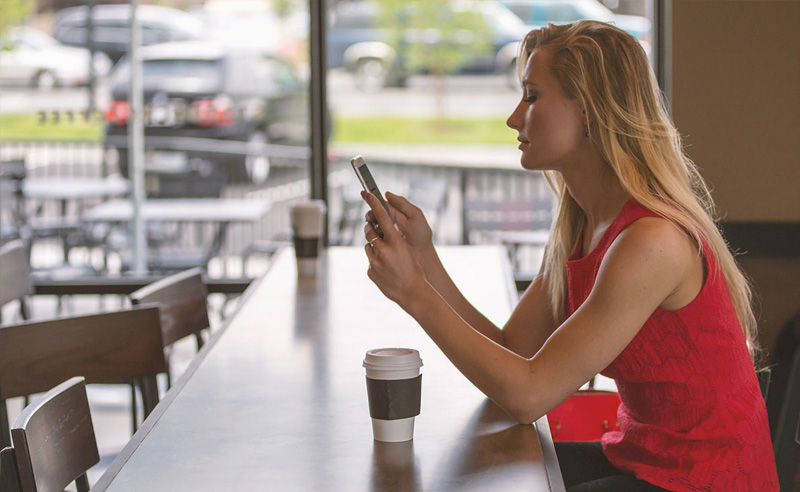Fiatal nő az asztalnál a telefonját nézi